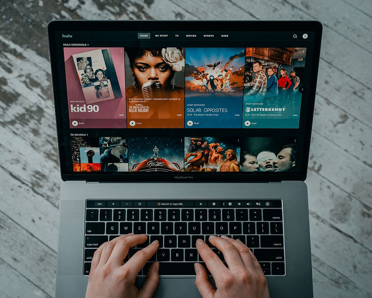 La mano en un portátil cuya pantalla está cubierta de contenidos de streaming de películas