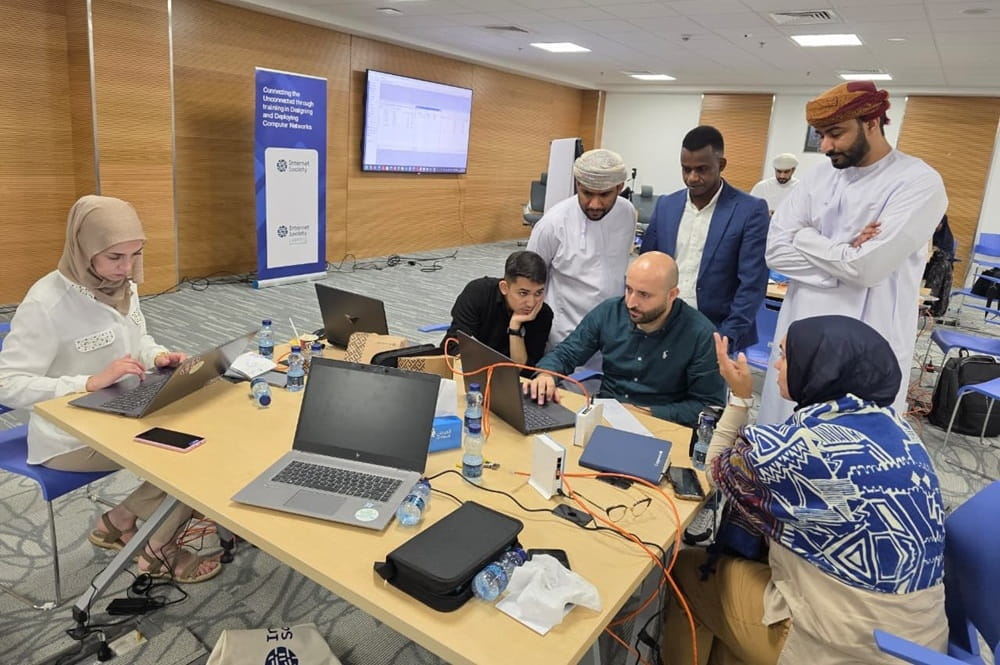 People standing around the desk and looking at laptops