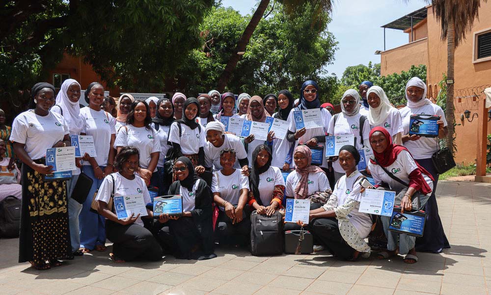 A large group of young women pose together outside, holding certificates